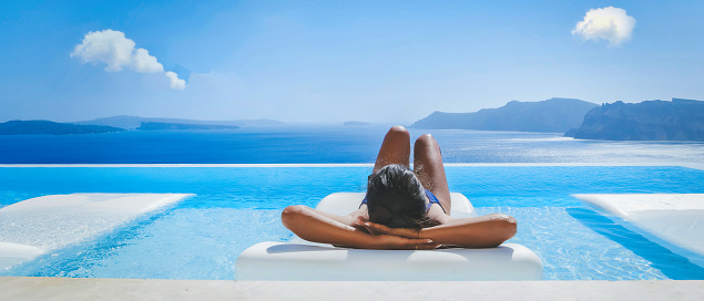 Young Asian women on vacation at Santorini relaxing in a swimming pool looking out over the Caldera ocean of Santorini, Infinity pool at Oia Greece, Greek Island Aegean Cyclades.