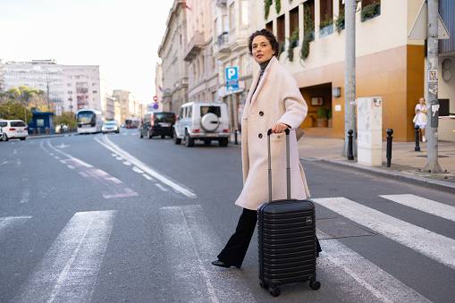Mid adult female entrepreneur pulling her luggage while crossing the road in the city.