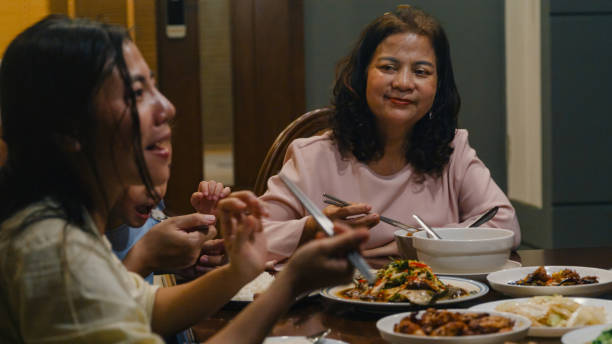 asian family eating chinese food and having fun dinner sitting at dining table at backyard outside home at night. multi-generation family enjoying spending together. - eating senior adult color image spaghetti imagens e fotografias de stock