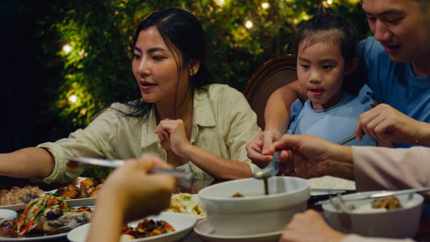 asian family eating chinese food and having fun dinner sitting at dining table at backyard outside home at night. multi-generation family enjoying spending together. - eating senior adult color image spaghetti imagens e fotografias de stock