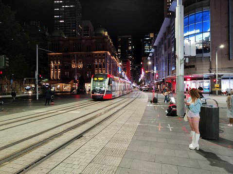 People on the sidewalks and tramway riding in the Sydney central business district at night, New South Wales, Australia.