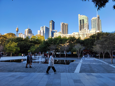 Sydney modern skyline viewed at Darling Harbor. People walking on the pedestrian zone in central Sydney.