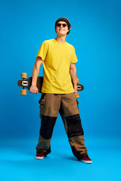 istock Young attractive man dressed in retro, reggae, rasta style and posing with skateboard against blue studio background. Concept of youth. 1830096384