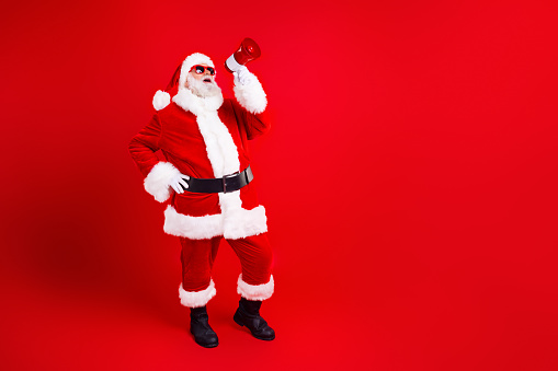 Full size photo of funky grandfather wear stylish santa costume hold megaphone screaming in empty space isolated on red color background.