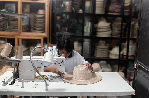 A young Hispanic woman is sewing a natural fiber hat with a machine in a traditional workshop in Guatemala