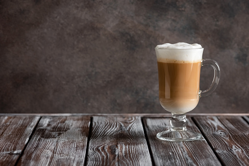 Latte coffee in a tall glass on a dark wooden table. Side view, copy space.