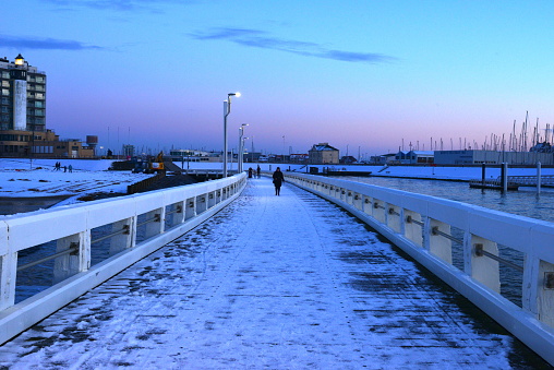 Blankenberge, West-Flanders, Belgium - December 02, 2023: Tourists in winter clothing walking on the illuminated beach pier covered with snow