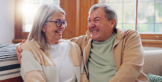 istock Senior couple, happiness and retired while laughing, talking and smile, couch and touch. Retirement, old age home and elderly in living room, couch and bonding together for quality time, hug or care 1830135261