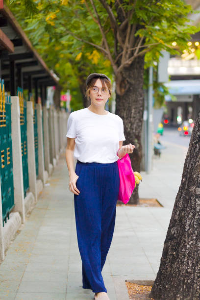 istock Thai transgender with cap and shopping bag is walking on sidewalk with trees 1830137992
