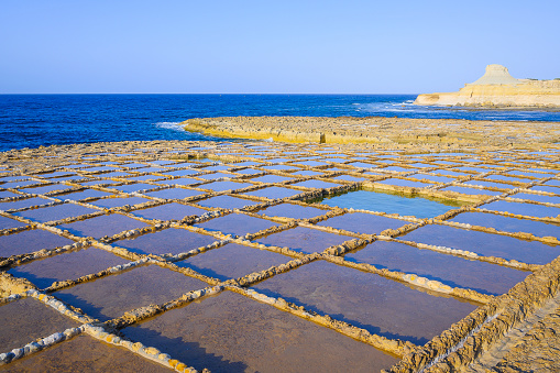 Gozo salt pans are an iconic cultural landmark.\nA salt pan is a shallow reservoir dug out of limestone rock to collect seawater. As the water evaporates, white salt crystals remain. The crystals are then dried and packed into salt pouches.\nThe most famous salt pans are in Xwejni Bay near Marsalforn. These salt pans are known for their picturesque view. These scenic 350 year old salt ponds are arranged in a chequerboard pattern and stretch about 3km along the coast. They are part of the centuries old Gozitan tradition of Sea-Salt production that has been passed down within certain families for many generations.\nXwejni Bay, Marsalforn, Gozo, Malta, Europe.