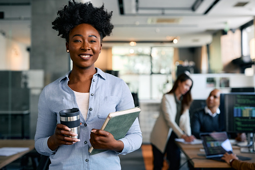 Happy African American graphic designer in the office looking at camera. Her colleagues are in the background.