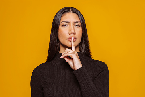 Portrait of a beautiful young latin american displeased girl showing silence gesture on camera.