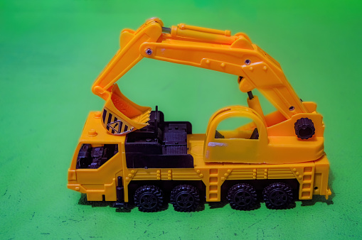a yellow toy miniature excavator on a flat green background