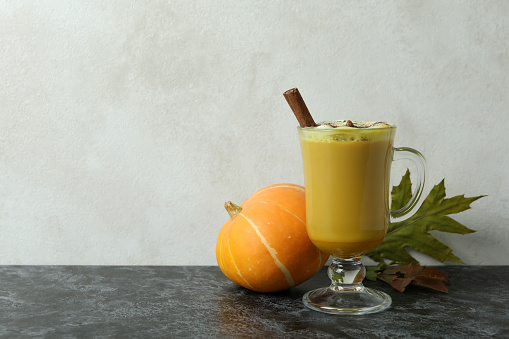 Glass of pumpkin latte, pumpkin and leaves on black smokey table