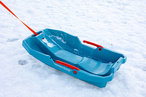 Empty blue plastic sled with a red rope lies on a snow-covered ground.Concept representing winter sports, childhood, leisure activities during the cold season, and family fun.Space for text
