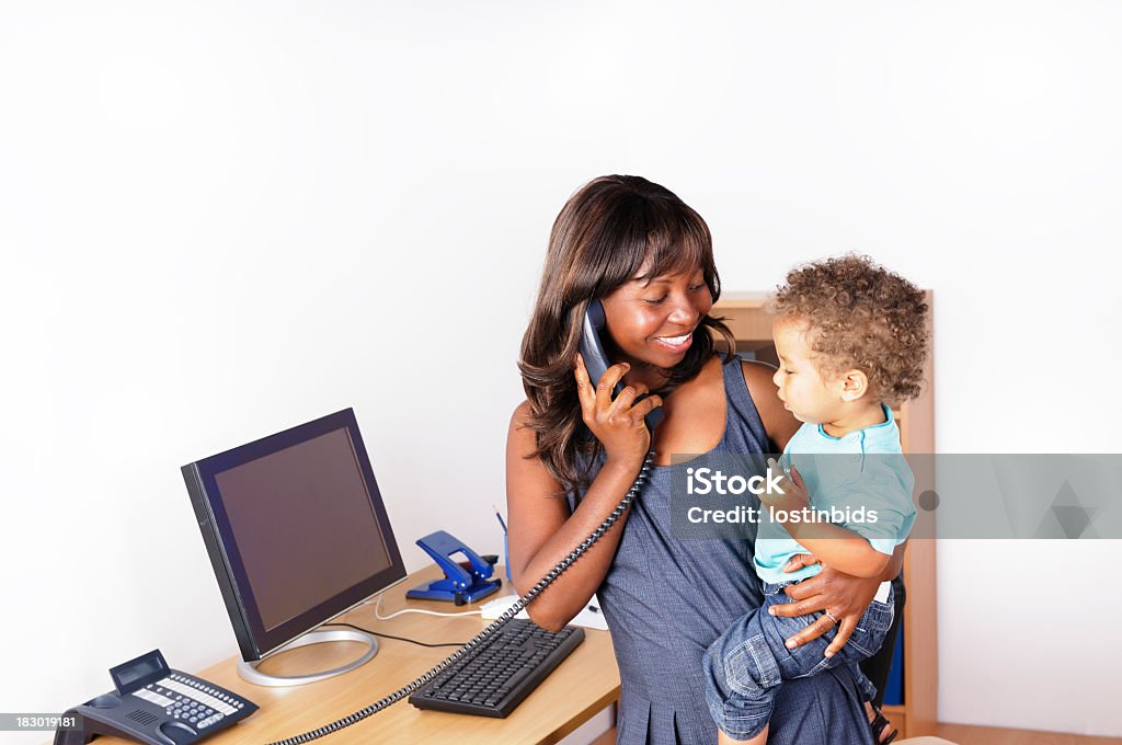African American Woman Holding Her Son While Phone Biracial baby/ toddler watching his mother while she is speaking on the telephone in a home office. Baby - Human Age Stock Photo