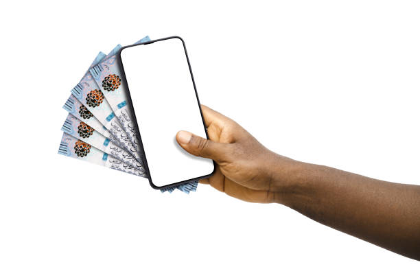 istock Black hand holding mobile phone with blank screen and Saudi Riyal notes 1830193662