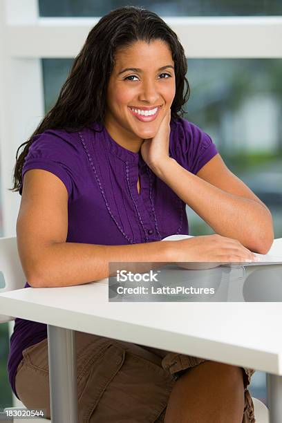 Foto de Sorrindo Feminino Sentado Atrás De Uma Escrivaninha Com A Reserva e mais fotos de stock de 30-34 Anos