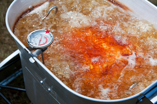 Close up image of a turkey frying to a nice crispy golden brown in an outdoor home deep fryer.  The Thermometer reads about 325 degrees Fahrenheit.  The oil is bubbling and rolling all over the yummy turkey.