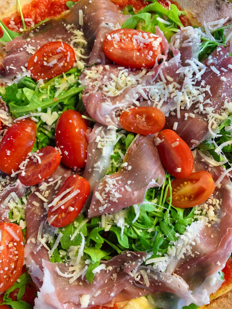istock Handcrafted pizza topped with smoked ham, fresh tomatoes, and arugula salad, generously sprinkled with Parmesan cheese. 1830216290