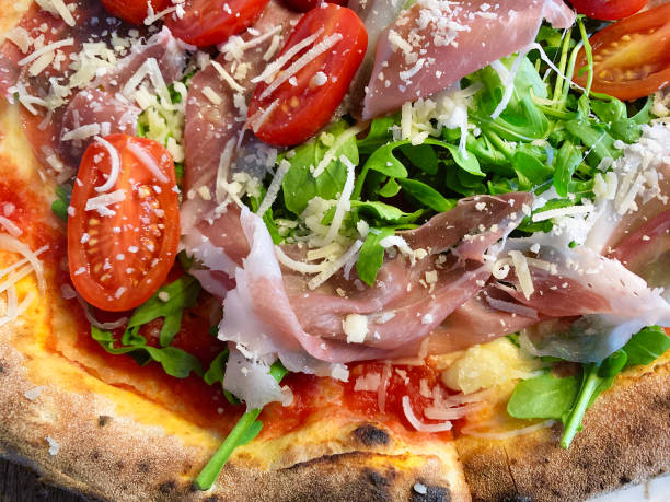 Handcrafted pizza topped with smoked ham, fresh tomatoes, and arugula salad, generously sprinkled with Parmesan cheese.
