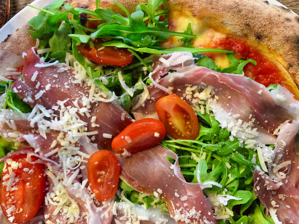 istock Handcrafted pizza topped with smoked ham, fresh tomatoes, and arugula salad, generously sprinkled with Parmesan cheese. 1830224503