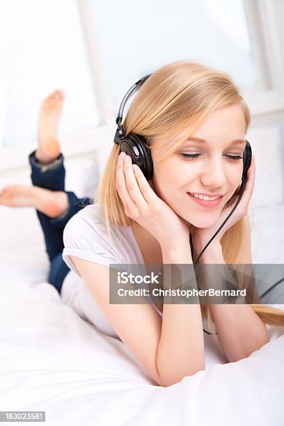 Joven Mujer Escuchando Música Con Auriculares En Foto de stock y más banco de imágenes de 18-19 años - 18-19 años, Acostado, Acostado boca abajo