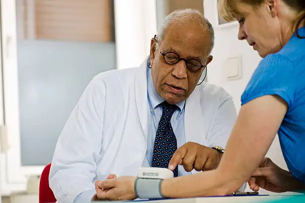 Older male doctor shows the blood pressure results to a female patient wearing a gauge on her wrist. Horizontal shot.