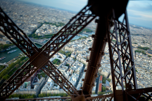 A view looking out through the structure and supports of the Eiffel Tower onto the city of Paris, France. Taken with a tilt-shift lens for miniature effect and selective focus running horizontally through the center of the frame down to the city below.