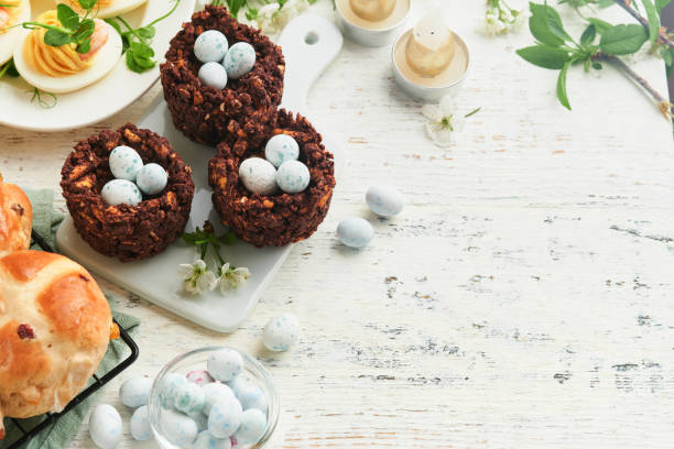Easter brunch or breakfast. Easter chocolate nest cake with chocolate candy eggs, traditional hot cross buns and deviled eggs with bouquets of blooming apple trees. Spring Easter holiday food concept.