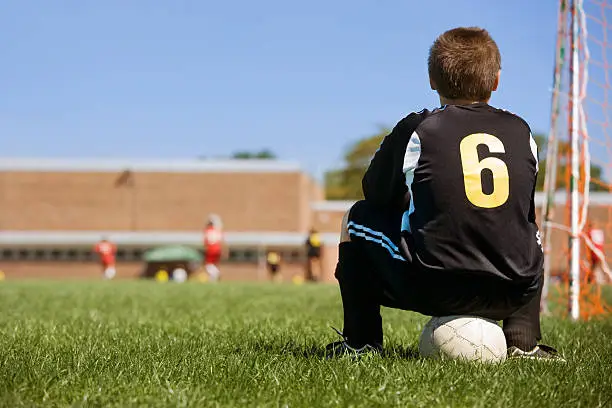 young boy watching soccer game from behind goal on sidelines.