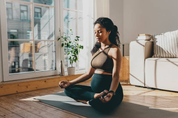 vue latérale d’une femme assise dans la posture du lotus sur le sol, pratiquant le yoga sur le sol à la maison, gardant les yeux fermés et faisant le signe mudra avec les mains, respirant profondément, atteignant le zen et l’harmonie - meditation photos et images de collection