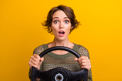 Photo of attractive young woman frightened hold rudder dressed stylish knitted khaki clothes isolated on yellow color background.