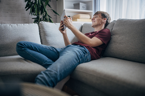 Young man using digital tablet while sitting on sofa at home.