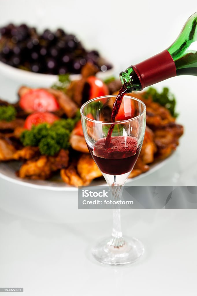 Vin rouge versé en bouteille, de la viande grillée en arrière-plan - Photo de Alcool libre de droits