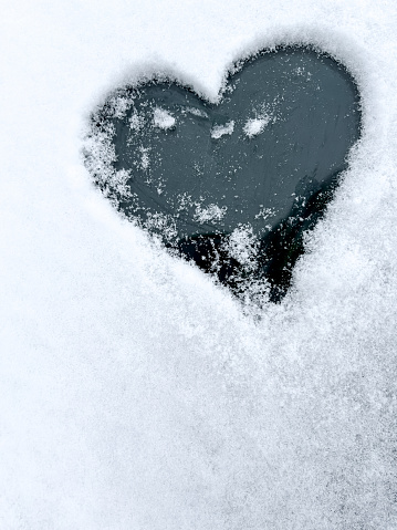 Heart shaped love sign drawn on snowy ice on a winter car window with copy space. Romantic background.