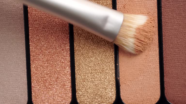 A palette with eye shadows and a makeup brush. Brush gains beige eyeshadows on pile to be used in make-up. Cosmetic swatch of eyeshadows, powder, bronzer or highlighter