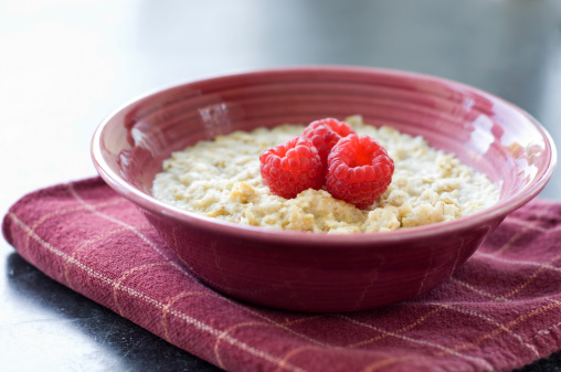 A bowl of fresh oatmeal with three raspberries.