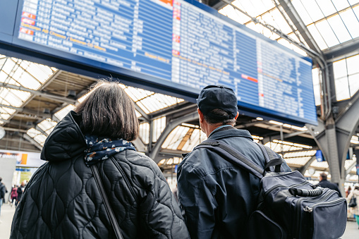 Senior tourist couple checking arrival and departure board at the Zurich's train station in Switzerland.