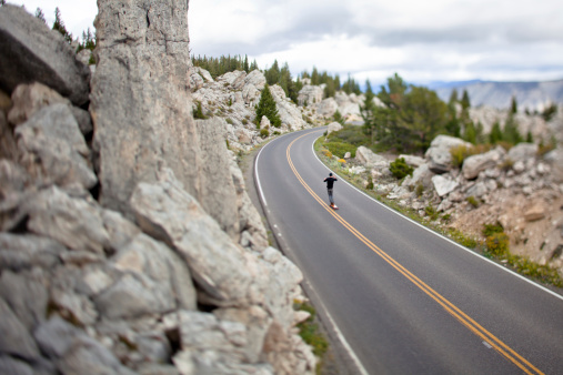 A hip long boarder (skater) cruises down a long stretch of paved road in Yellowstone National Park.