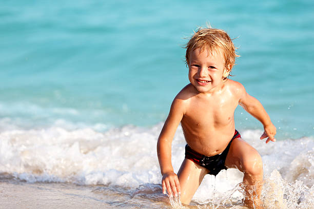 Happy little boy having fun on the beach, by the sea.