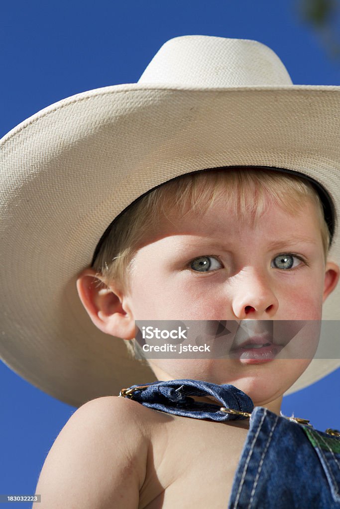 Cute Young Cowboy With Large Hat A cute 2 year old boy in his large cowboy hat looks down from a high locations. Chickenlypse 2010 Bib Overalls Stock Photo