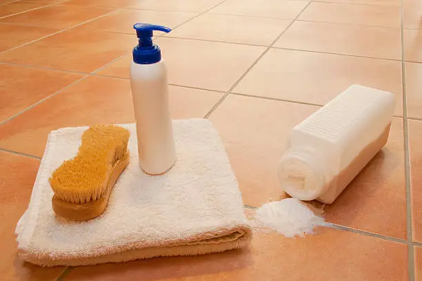 Wellness theme: White folded towel, natural bath brush, spilled bath salt and bottle with liquid soap on shiny italian style floor tiles, selective focus. Horizontal orientation. The image has been shot full frame and close up. The Dimensions of the photo are 4220 px × 2803 px.