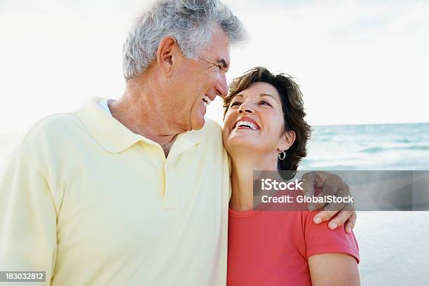 Foto de Sorridente Casal De Aposentados Com Os Braços Em Uma Praia e mais fotos de stock de 40-49 anos