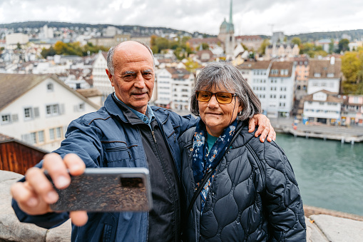 Senior couple taking a selfie using a smartphone with view of Limmat river in Zurich, Switzerland.