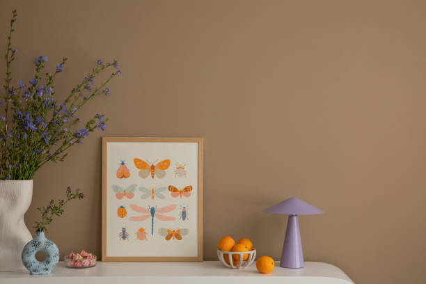 istock Living room interior with mock up poster frame, copy space, white sideboard, purple lamp, stylish vase with flowers, bowl with orange and personal accessories. Home decor. Template. 1830334314