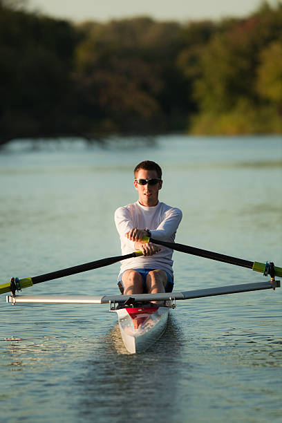 Sculling Athletic Rower Sport Rowing a Nautical Vessel on Lake A young athletic man rowing, sculling on a boat, a nautical vessel rowboat, in the late afternoon sun on Lake of the Isles, Minneapolis, Minnesota, USA. individual event stock pictures, royalty-free photos & images
