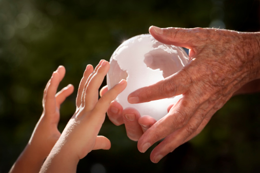 Close up of a crystal globe passing from an old woman's hand to the little child's outstretched hands in front of a dark foliage defocused background. Small amount of digital noise added.Related pictures: