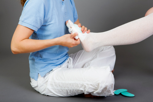 Close up of a young physiotherapist applying a compression bandage on the foot of a young woman. Physical Therapy. A very specialised type of massage called manual lymphatic drainage (MLD) is an important part of the treatment of lymphoedema. This kind of compression bandages are part of this treatment. Studio shot. Grey background. XXXL (Canon Eos 1Ds Mark III)