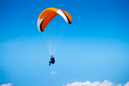 A wide angle view of a paraglider flying high in the sky against a blue background. Space for copy and text. ProPhoto RGB profile for maximum color fidelity and gamut.